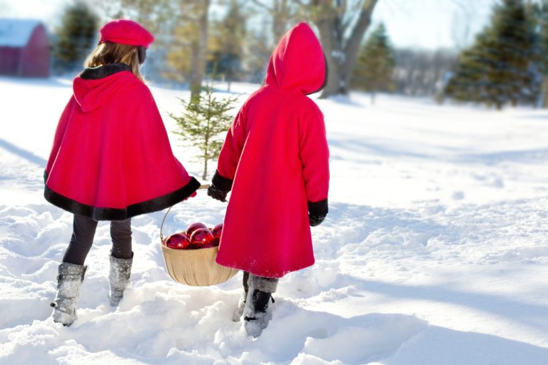 two girls in red winter coats walking through snow with ornament basket